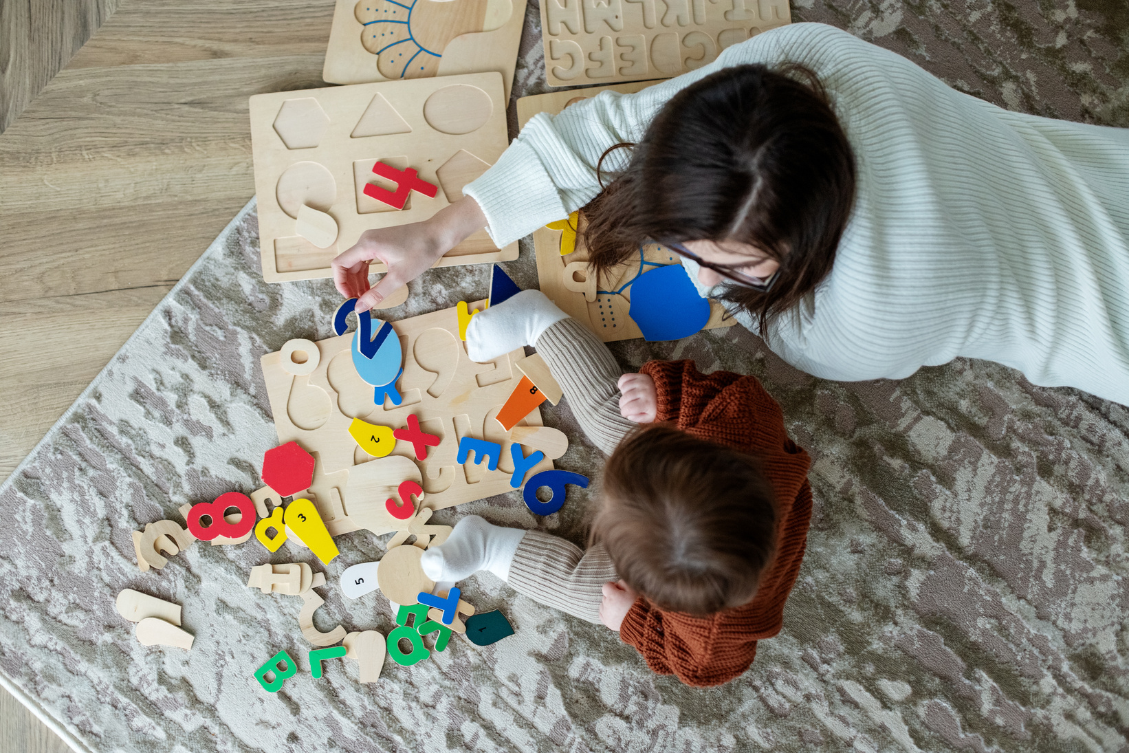 Mother and little daughter play educational games on rug in