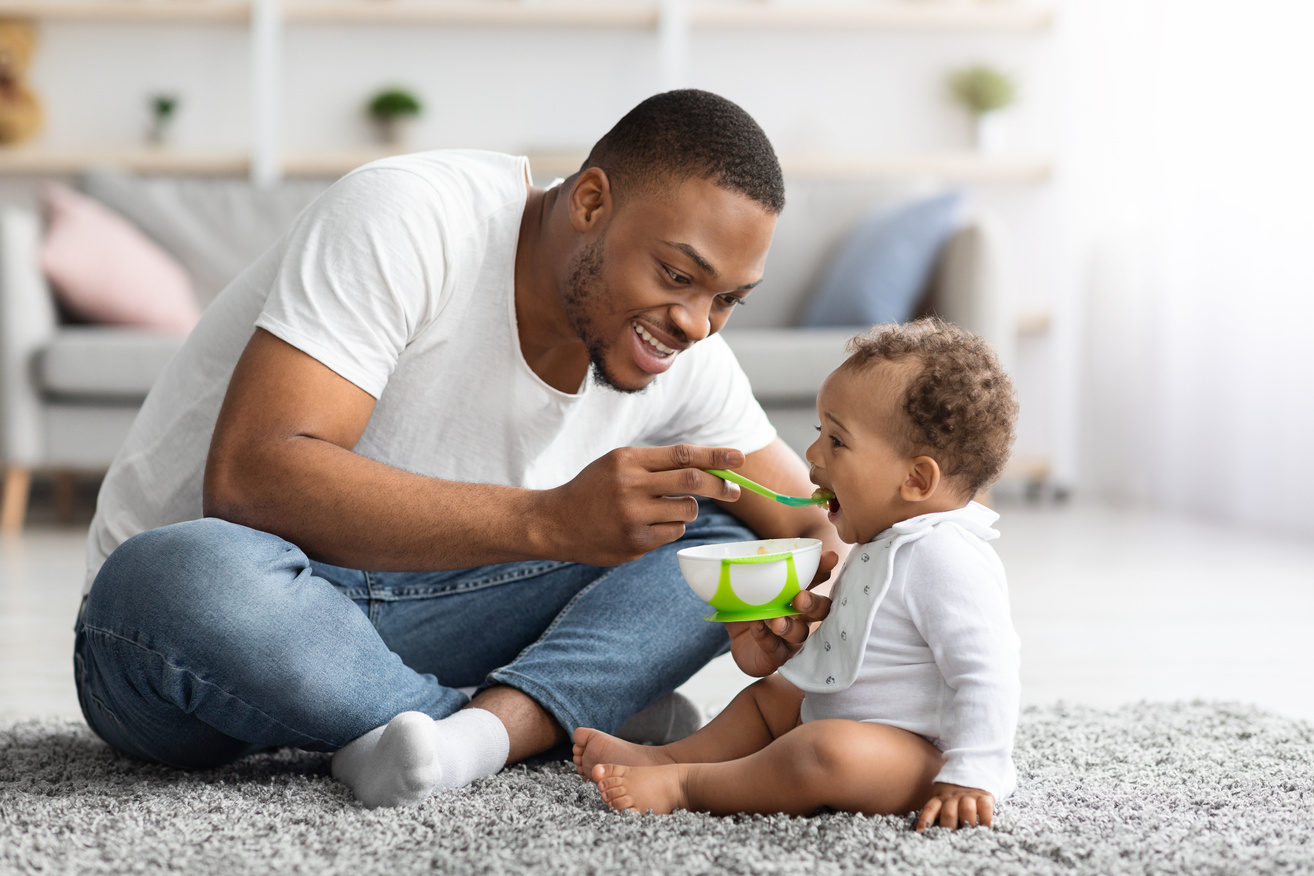 Childcare Concept. Caring Young Black Father Feeding Adorable Baby Son at Home